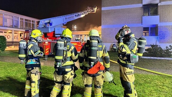 Vier Feuerwehrmänner stehen mit Helm und Atemflasche in der Nacht vor einer ausgefahrenen Feuerwehrleiter. © KFV Pinneberg 