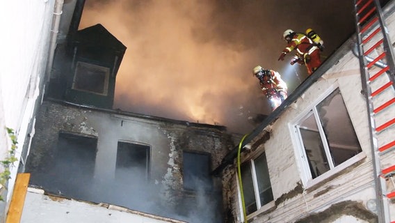 Zwei Feuerwehreinsatzkräfte stehen auf einem Dach in Flensburg und löschen einen Dachstuhlbrand © Westküsten-News 