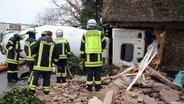 Ein Betonmischer liegt auf der Seite in einer durchbrochenen Hauswand, im Vordergrund stehen Einsatzkräfte der Feuerwehr. © Westküsten News Foto: Florian Sprenger