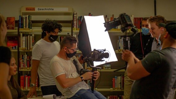 Louis Bennies mit der Kamera am Filmset im Hintergrund hält eine Person ein Licht fest. Louis Bennies mit der Kamera am Filmset im Hintergrund hält eine Person ein Licht fest. © Louis Bennies