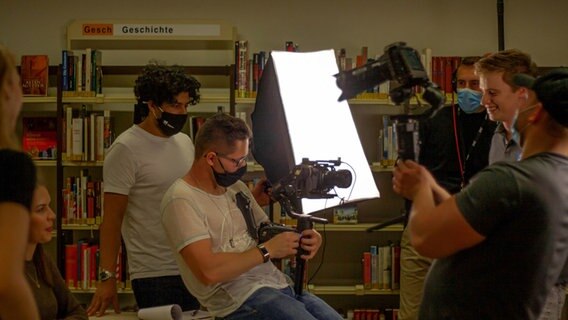 Louis Bennies mit der Kamera am Filmset im Hintergrund hält eine Person ein Licht fest. © Louis Bennies 