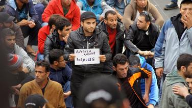 Ein Flüchtling hält am 08.09.2015 auf dem Lübecker Hauptbahnhof ein Schild mit der Aufschrift "Angela Merkel, help us" in die Luft. © NDR Foto: Katrin Bohlmann