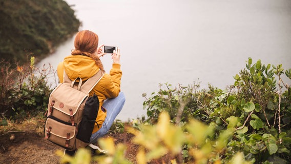 Eine junge Frau fotografiert einen See. © Imago Images Foto: Westend61