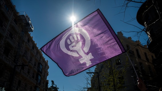 Eine Demonstrantin hält eine Fahne mit feministischem Symbol in die Luft. © Carlos Gil / picture alliance Foto: Carlos Gil