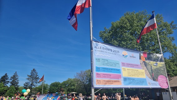 Auf einem großen bunten Plakat stehen mehrere Veranstaltungen im Freibad Quickborn für diesen Sommer. Im Hintergrund sind Menschen auf einer Wiese. © Doreen Pelz 