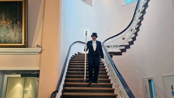 Ein Mann steht mit einem Zepter in der Hand auf einer Treppe in der "Lübecker Loge". © NDR Foto: Julian Marxen