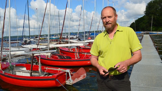 Helge Wiederich steht auf der Steganlage der Segelschule Plön und schaut in die Kamera. Helge Wiederich steht auf der Steganlage der Segelschule Plön und schaut in die Kamera. © NDR Foto: Anne Passow