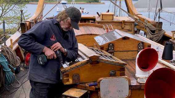 Arved Fuchs steht auf einem Schiff und hält eine Bohrmaschine. © NDR Foto: Lena Haamann