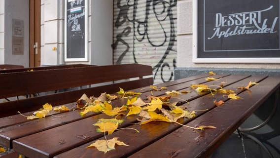 Eine Tischgarnitur vor einem geschlossenen Restaurant mit Laub auf dem Tisch. © imago images / Seeliger 