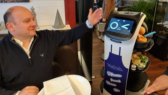 Ein Gast im Hafenrestaurant Grömitz strechelt den Gastro-Roboter. © NDR Foto: Julian Marxen