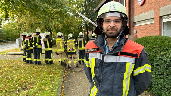 Ein Mann posiert in Feuerwehruniform vor einer Feuerwehrwache. © NDR Foto: Johannes Tran