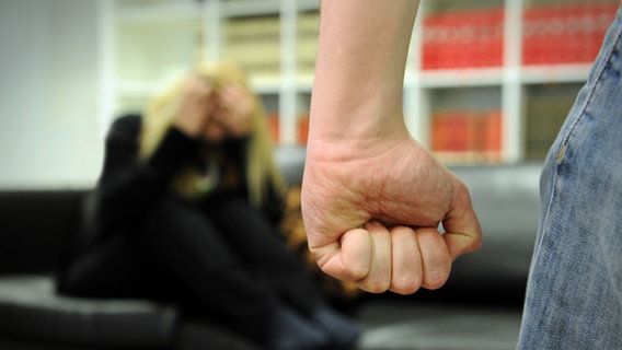 Ein Mann bedroht eine auf dem Sofa zusammengekauert sitzende Frau mit seiner Faust. (Themenbild) © picture-alliance / dpa Foto: Jan-Philipp Strobel