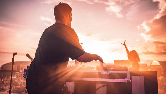 Ein DJ legt auf einer Bühne bei Sonnenuntergang auf. © MxM Photo Foto: MxM Photo