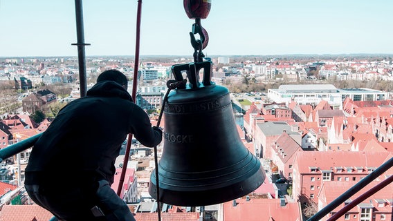 Ein Arbeiter zieht eine Glocke am Turm der Marienkirche in Lübeck mit einem Kran hoch. © dpa-Bildfunk Foto: Daniel Bockwoldt/dpa-Bildfunk