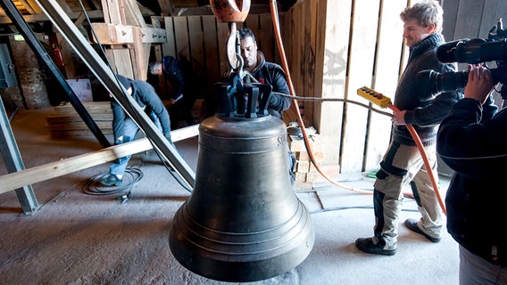 Arbeiter stehen um eine Glocke herum, die mit einem Kran in den Turm der Lübecker Marienkirche gezogen wird. © dpa-Bildfunk Foto: Daniel Bockwoldt/dpa-Bildfunk