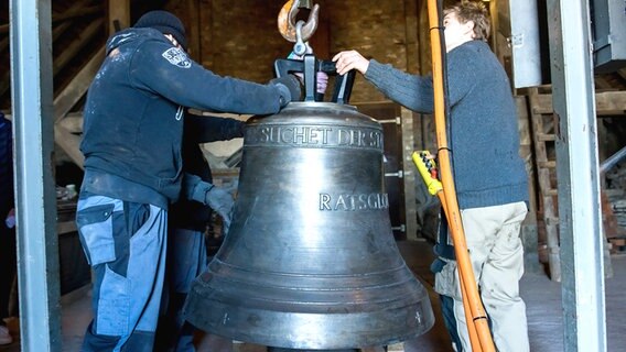 Zwei Arbeiter überprüfen die Befestigung einer Glocke, die in den Turm der Lübecker Marienkirche gezogen wird. © dpa-Bildfunk Foto: Daniel Bockwoldt/dpa-Bildfunk