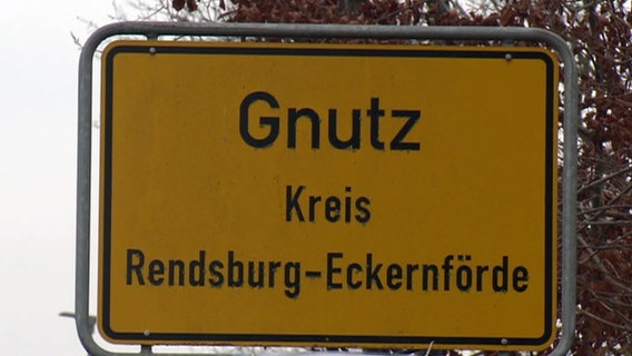 Das gelbe Orsschild von Gnutz im Krei Rendsburg-Eckernförde steht vor graem Himmel. © NDR 