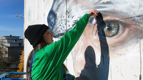 Eine Frau besprüht mit einer Graffiti-Dose eine Hauswand. © NDR Foto: Johannes Tran