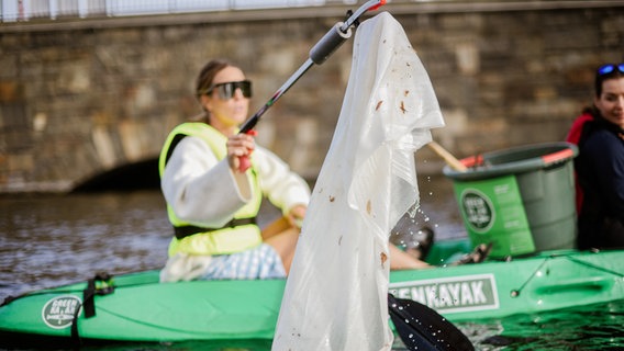 Eine "Green Kayak" Fahrerin hält einen Plastikmüllbeutel in die Kamera. © Green Kayak 