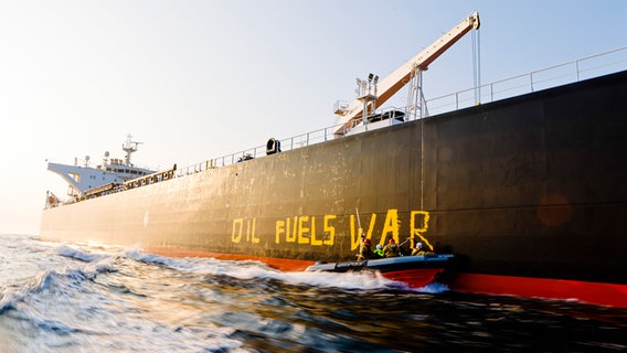 Aktivisten der Umweltorganisation Greenpeace malen den Schriftzug «Oil fuels war» von einem Schnellboot aus auf einen Schiffsrumpf. © dpa-Bildfunk Foto: Frank Molter/dpa