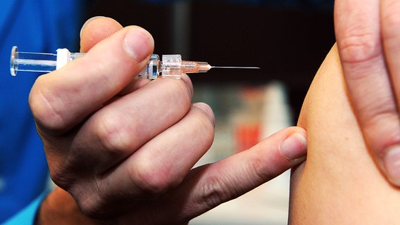 Arzt im blauen Kittel setzt eine Spritze mit Impfstoff an den Arm eines Patienten © picture alliance / dpa Foto: Caroline Seidel