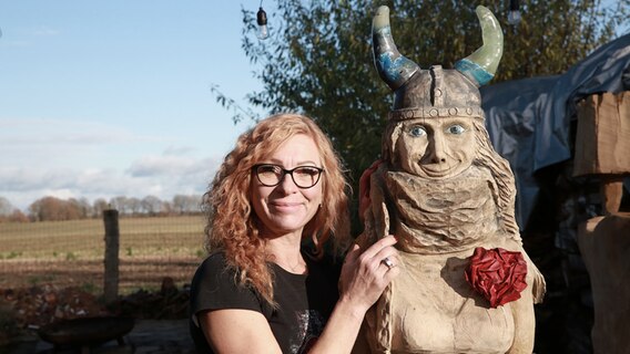 Kettensägen-Künstlerin Birgit Waniorek steht neben der von ihr gestalteten Skulptur "Schleswig-Holsteinchen". © NDR Foto: Christoph Klipp