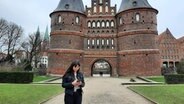 Eine junge Frau steht vor dem Holstentor und blickt auf ihr Handy.  Foto: Lina Bande