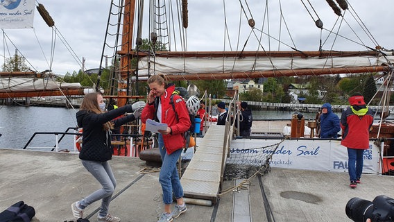Zwei junge Frauen fallen sich weinend in die Arme. Im Hintergrund liegt der Segler "Thor Heyerdahl".  Foto: Sebastian Parzanny