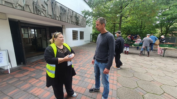 Eine Frau mit gelber Warnweste und ein Mann stehen vor dem Eingang der Sozialkirche in Kiel-Gaarden. © NDR Foto: Sebastian Parzanny