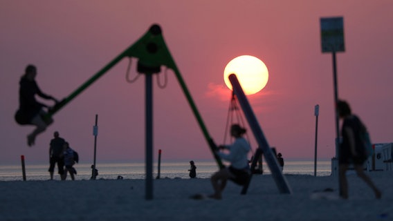 Sonnenuntergang über dem Meer, Personen Schaukeln im Vordergrund © dpa Foto: Bodo Marks