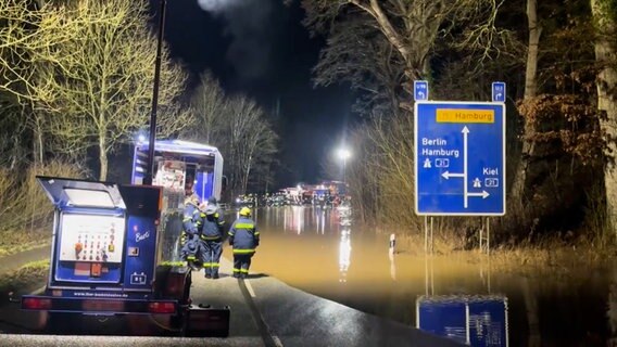 Mehrere Einsatzkräfte stehen an einer überschwemmten Straße. © TV-Elbnews 