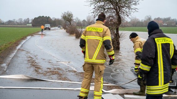 Mehrere Einsatzkräfte stehen mit einer Pumpe an einer überfluteten Straße. © 5NEWS 