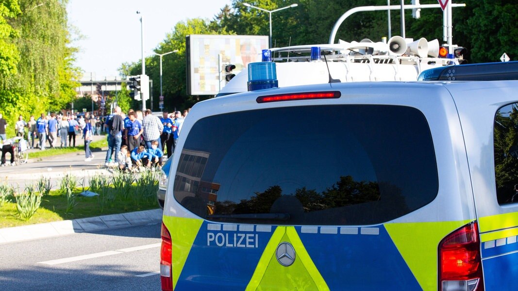 Hinter einem Polizeiauto laufen Holstein Kiel Fans in Richtung Stadion.