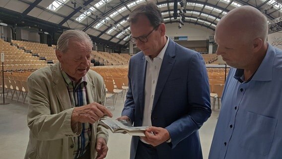 Herbert Möller (l.) steht neben dem dem Oberbürgermeister Olaf Taurus (m.) und amtierenden Geschäftsführer der Holstenhallen Dirk Iwersen (r.). © NDR Foto: Cassandra jane Arden