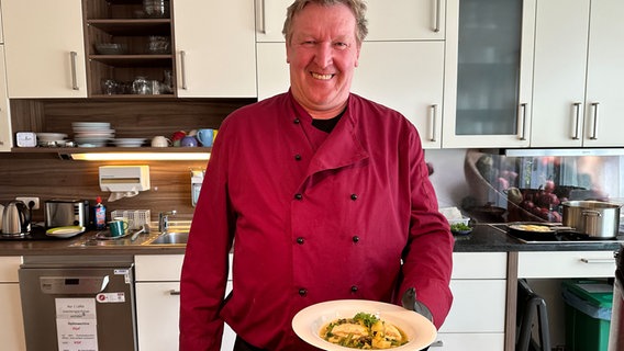 Ein Mann steht in einer Küche und präsentiert einen Teller mit Essen. © NDR Foto: Johannes Tran