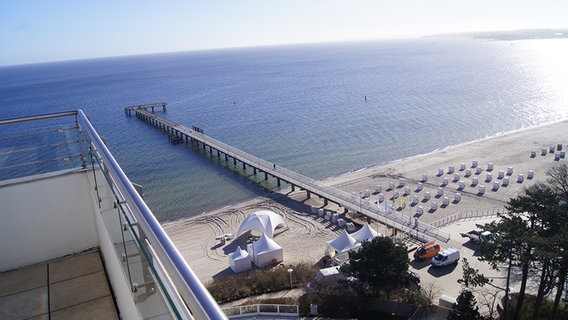 Von einer Terrasse mit Meerblick aus sind der Steg, Strand und mehrere Strandkörbe zu sehen. © NDR Foto: Hauke von Hallern