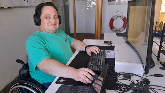 Webdesigner Paul Sznabel sitzt im Rollstuhl vor einem Arbeitstisch mit einem großen Monitor. © NDR Foto: Astrid Wulf