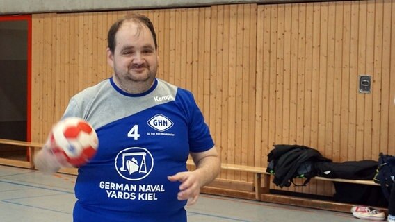 Der Handballer Patrick Kronshagen hält einen Ball in der Hand während er in die Kamera lächelt. © NDR Foto: Samir Chawki