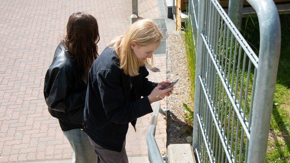 Zwei Schülerinnen stehen an einer Treppe und blicken auf ihre Smartphones. © NDR Foto: Lisa Pandelaki