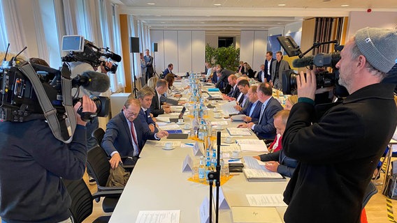 Vertreter der Kommunen sitzen bei einem Integrationsgipfel an einem Tisch, davor stehen zwei Kameramänner © NDR Foto: Fabian Boerger