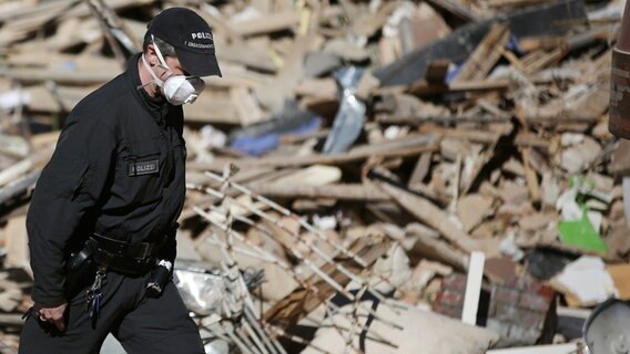 Ein Polizist mit Mundschutz steht in den Trümmern eines eingestürzten Hauses in Itzehoe © dpa Bildfunk Foto: Axel Heimken