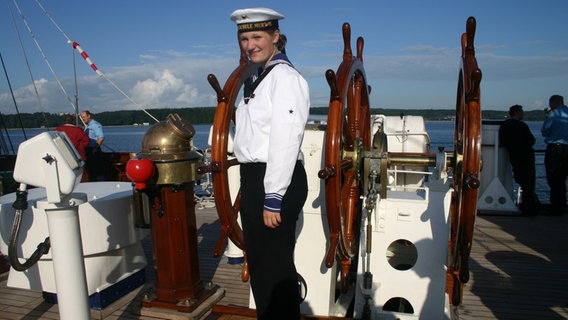 Matrosin Jenny Böken steht vor dem Steuerrad des Segelschiffs Gorch Fock. © Uwe Böken Foto: Uwe Böken