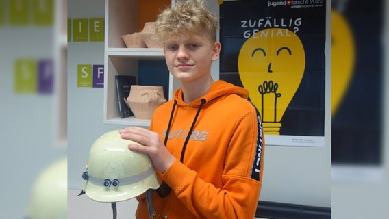 Ein Jugendlicher hält einen Feuerwehrhelm in die Kamera.  Foto: Stella Kennedy