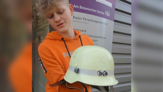 Ein Jugendlicher hält einen Feuerwehrhelm in die Kamera.  Foto: Stella Kennedy