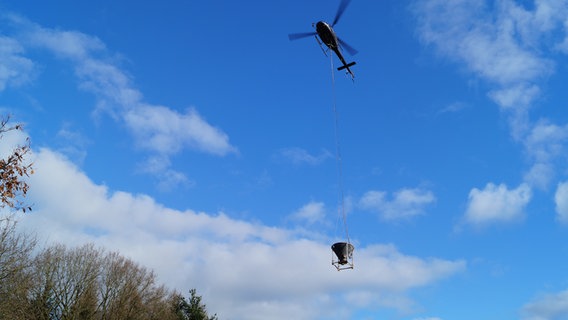 Ein Hubschrauber fliegt mit Kalkbehälter zum durch die Luft.  Foto: Jelto Ringena