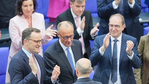 Der scheidende Bundeskanzler Olaf Scholz (M, von hinten, SPD) gratuliert dem neu gewählten Bundeskanzler Friedrich Merz (M, CDU) zu seiner Wahl. im Bundestag. Daneben applaudieren Jens Spahn (l, CDU), Unionsfraktionsvorsitzender, designierter und Alexander Dobrindt (r, CSU), designierter Bundesinnenminister. Der Kanzlerkandidat von CDU, CSU und SPD, Merz, erhielt im zweiten Wahlgang die nötige Stimmenzahl. © dpa-Bildfunk Foto: Michael Kappeler