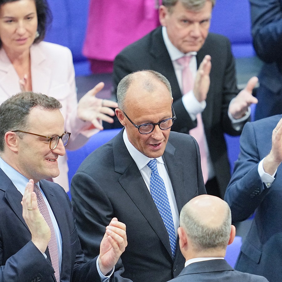 Der scheidende Bundeskanzler Olaf Scholz (M, von hinten, SPD) gratuliert dem neu gewählten Bundeskanzler Friedrich Merz (M, CDU) zu seiner Wahl. im Bundestag. Daneben applaudieren Jens Spahn (l, CDU), Unionsfraktionsvorsitzender, designierter und Alexander Dobrindt (r, CSU), designierter Bundesinnenminister. Der Kanzlerkandidat von CDU, CSU und SPD, Merz, erhielt im zweiten Wahlgang die nötige Stimmenzahl. © dpa-Bildfunk Foto: Michael Kappeler