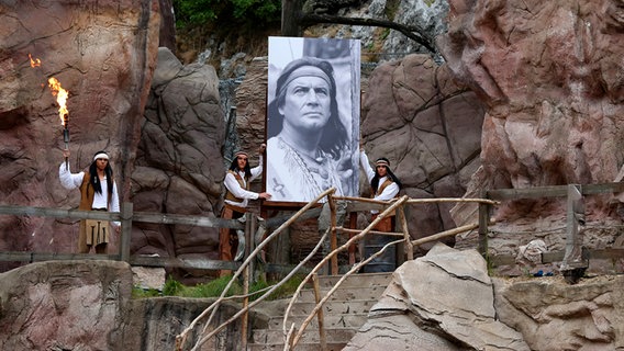 Ensemblemitglieder halten ein Foto von Schauspieler Pierre Brice hoch. Danach startet die Premiere von "Im Tal des Todes" im Rahmen der 64. Karl-May-Spiele auf der Bad Segeberger Freilichtbühne am Kalkberg 2015. © picture alliance / Geisler-Fotopress Foto: Sebastian Gabsch