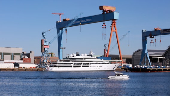 Im Kieler Hafen liegt die große Yacht "Katara" bei blauem Himmel. Ein Boot davor zeigt die Dimensionen der Yacht. © NDR Foto: Henrike Wiesemann