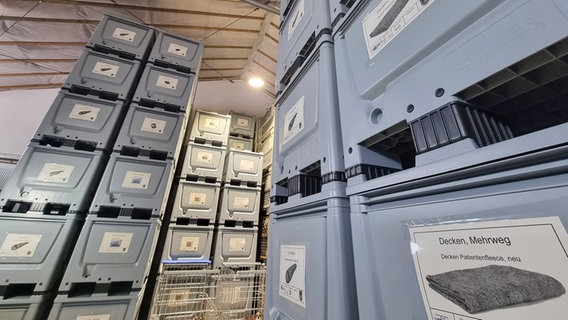 Graue Kisten mit Decken und Schlafsäcken liegen in einem Lagerraum. © NDR Foto: Julian Marxen